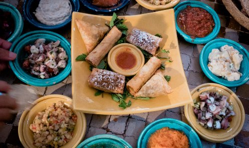 Table with 6 plates of Meze-style dips and bread.  